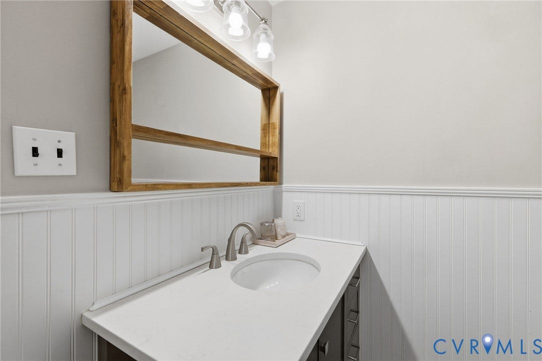 1109 Swissvale Place, Henrico, VA 23229 Beadboard wainscoting, integrated sink, wood-framed mirror, vanity with storage, and wall-mounted lighting fixture