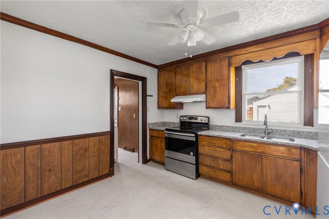 Wood-finish cabinetry with light-toned countertops, stainless steel range, and a ceiling fan with integrated lighting