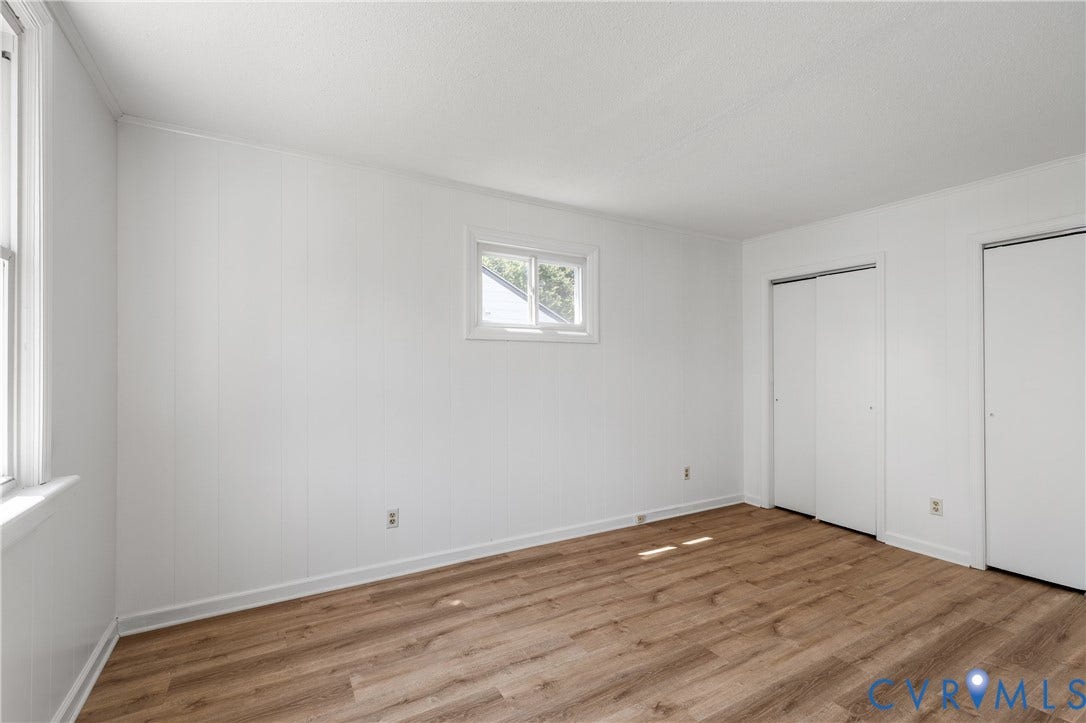 Wood-finish flooring, white paneled walls, and two windows provide natural light