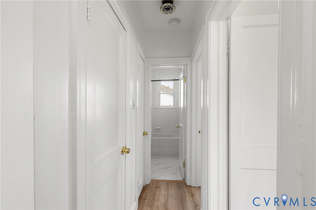 Hallway featuring wood-finish flooring, white paneled doors, and brass hardware