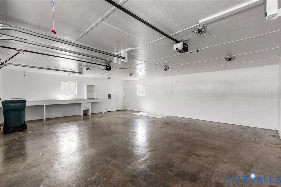 Spacious garage with concrete flooring, built-in workbench, overhead lighting, and white paneled walls