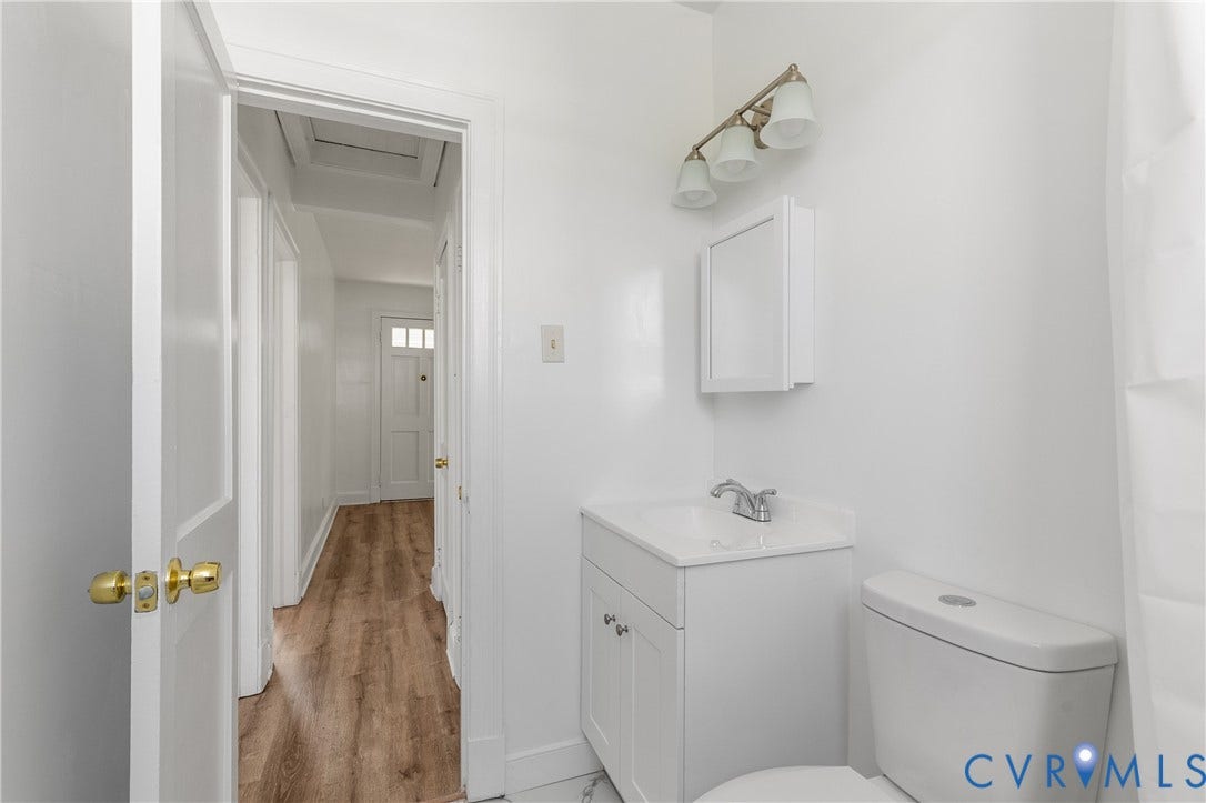 White vanity with an integrated sink and chrome faucet, surface-mounted medicine cabinet, three-light vanity fixture, and wood-finish flooring in the hallway