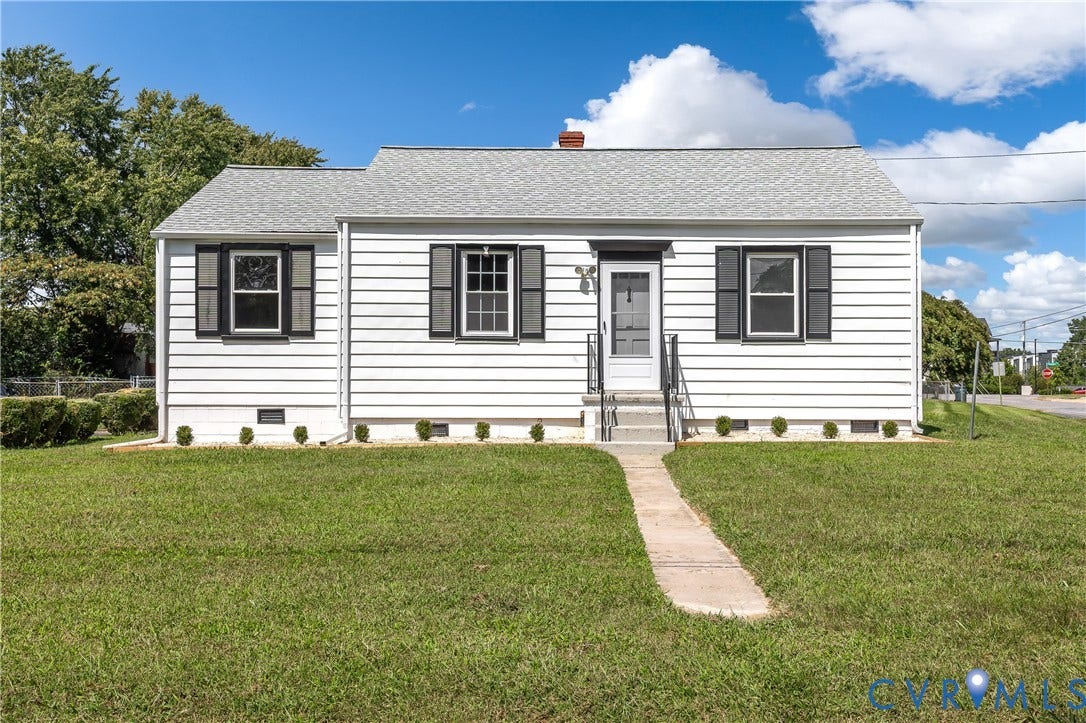 Classic white vinyl-sided cottage featuring a gabled roof with asphalt shingles, black-trimmed windows with shutters, and a centered front entrance with concrete steps