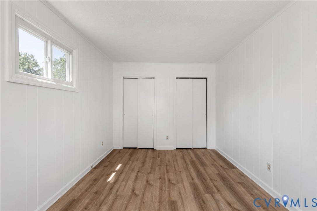 Wood-finish flooring with white paneled walls, a single window, and two closet systems
