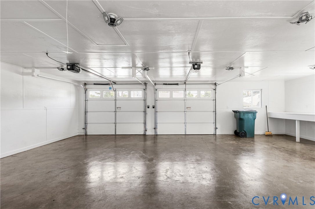 Two white paneled garage doors with upper window inserts, concrete flooring, overhead lighting, and built-in workbench