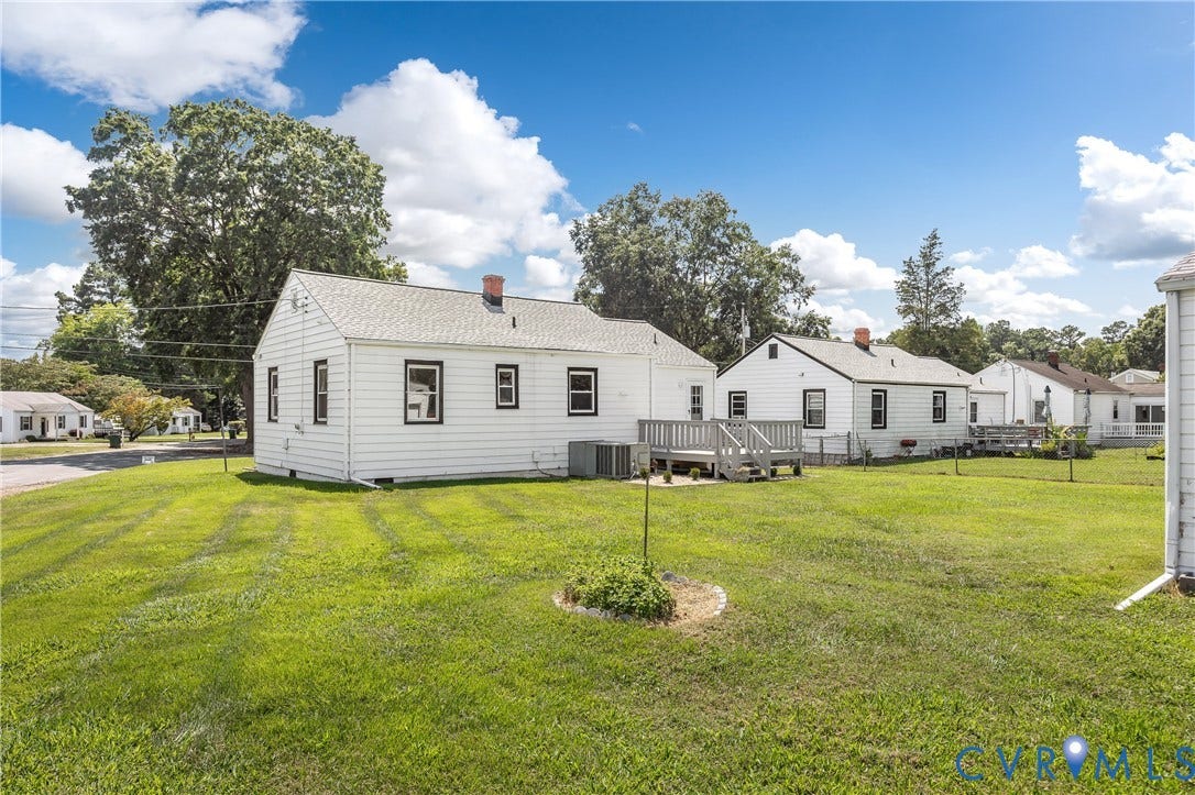 Expansive rear yard featuring green grass, a wooden deck, and mature perimeter trees