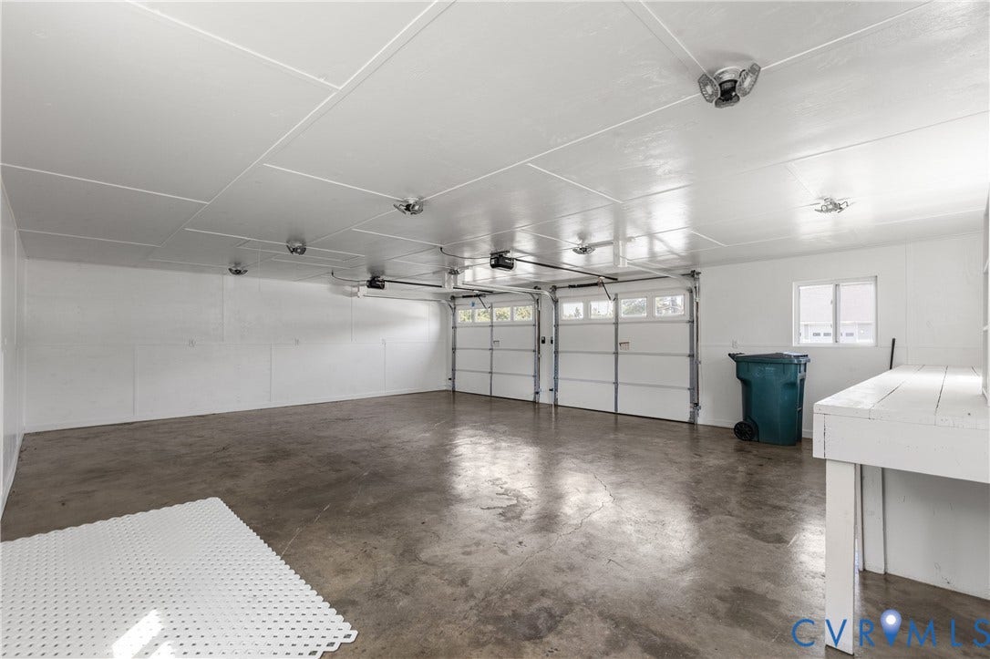 Spacious garage featuring two overhead doors, concrete flooring, overhead lighting, and a built-in workbench