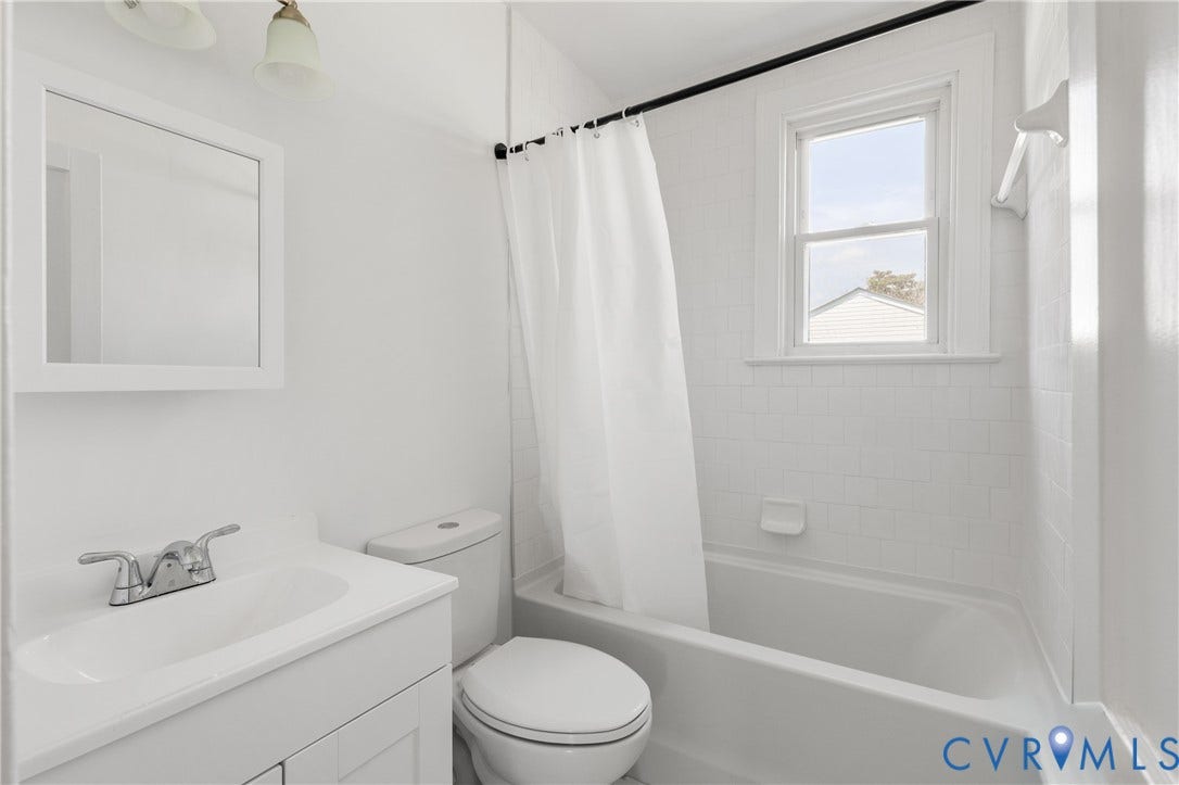 White vanity with integrated sink, chrome faucet, framed mirror, white subway tile shower surround, and a tub with an operable window