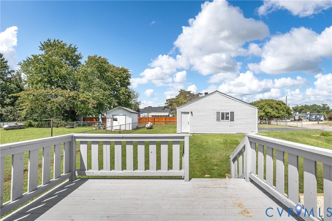 Deck with railings overlooking a grassy yard, featuring a white detached outbuilding and a storage shed