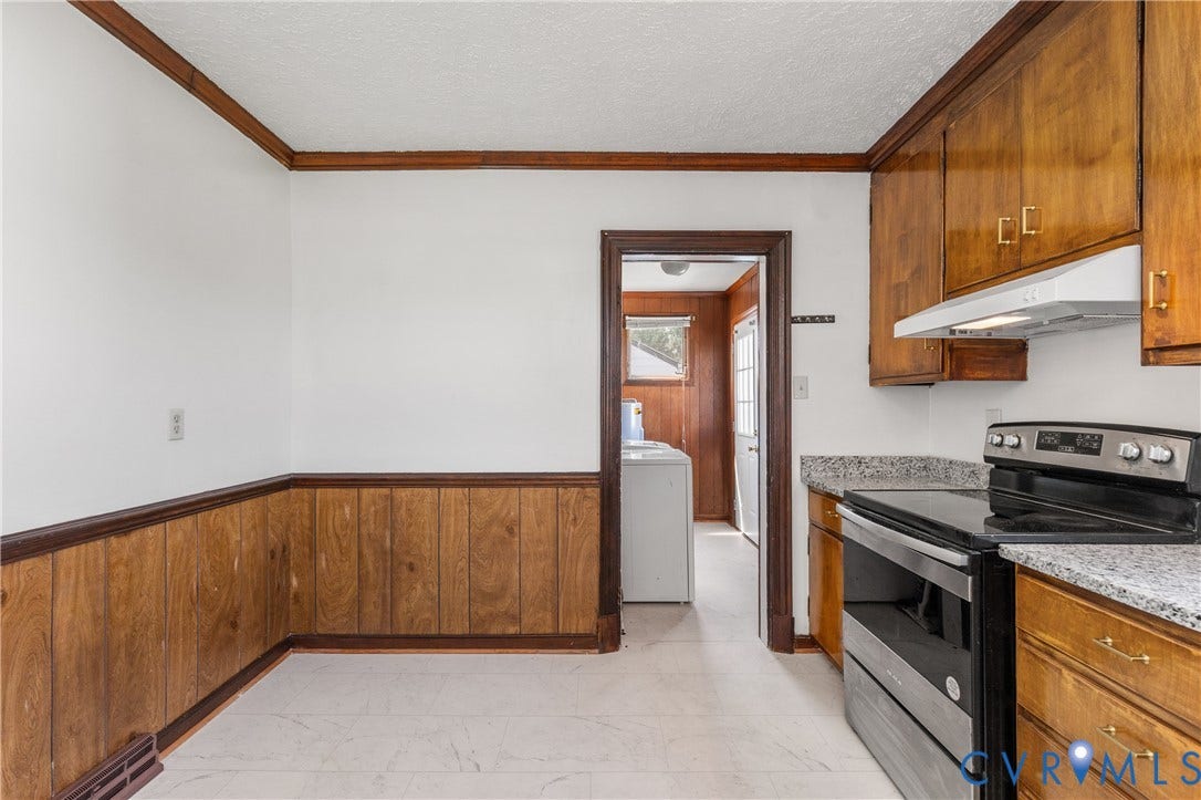 White walls with wood paneling, wood-finish cabinetry, light-toned flooring, and a stainless steel range with overhead ventilation