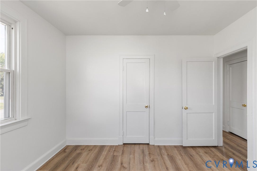 Recessed window with white trim, wood-finish flooring, and white interior doors with brass hardware