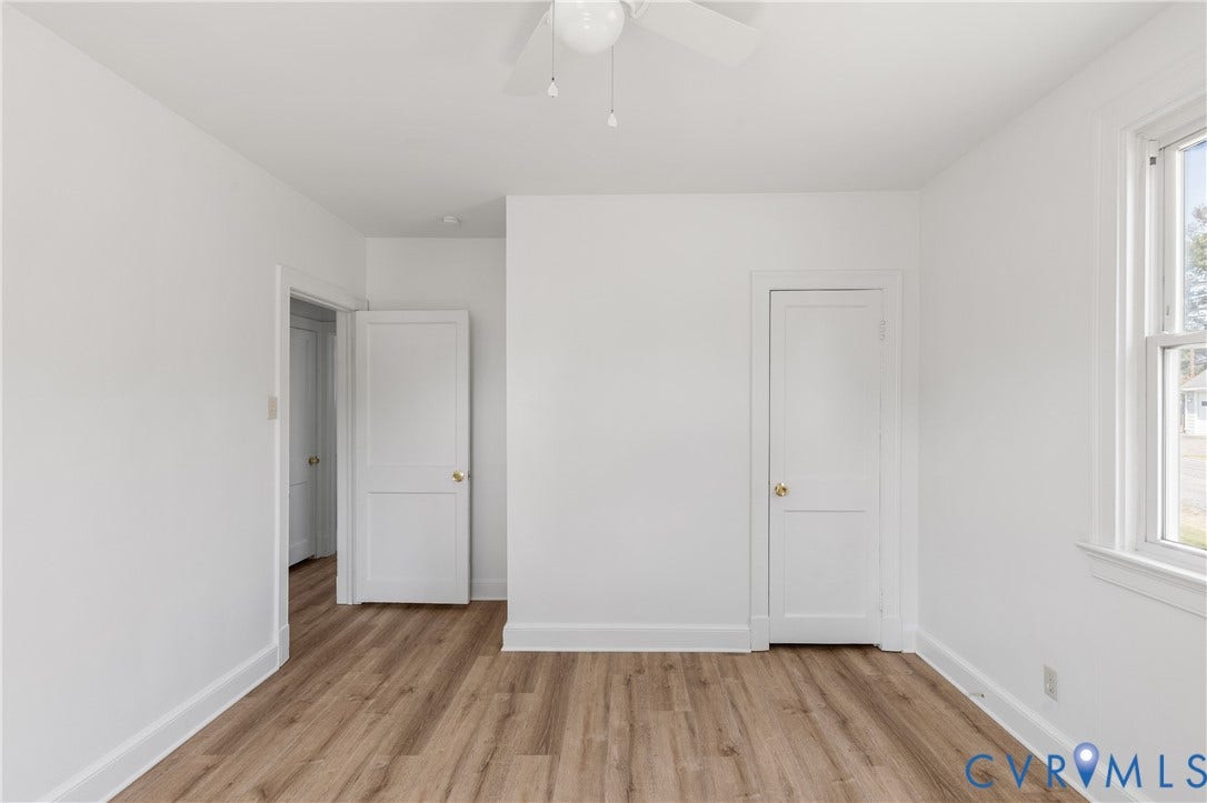 Wood-finish flooring, white walls, white trim, ceiling fan, and a window with white casing