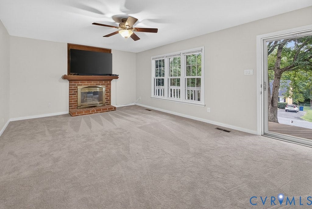 3112 Castlebury Drive, Chester, VA 23831 Spacious room featuring a brick fireplace with a wood mantle, ceiling fan, carpeted flooring, and a sliding glass door opening to an exterior deck