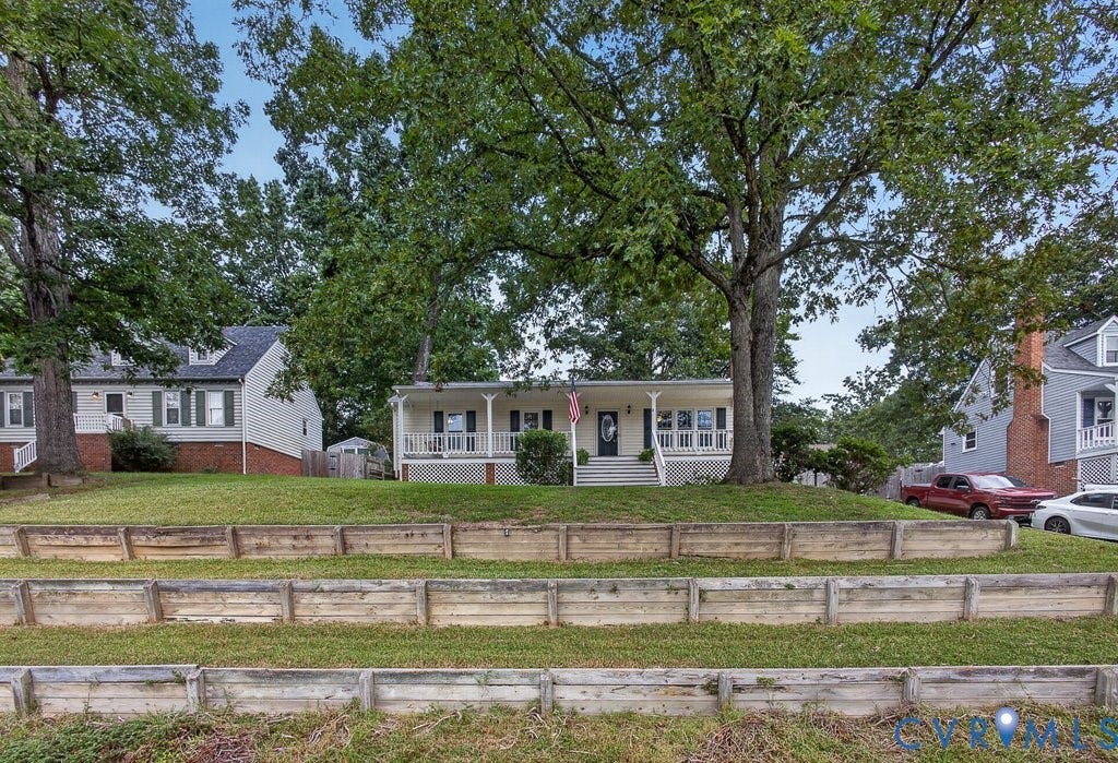 3112 Castlebury Drive, Chester, VA 23831 White facade property featuring a full-width front porch with railings, mature shade trees, and a terraced front yard with retaining walls