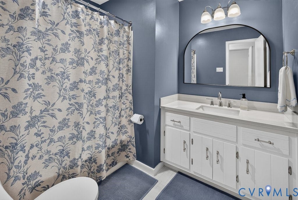 3112 Castlebury Drive, Chester, VA 23831 White vanity with a single basin sink and brushed nickel faucet, large arched mirror, and a three-light vanity fixture