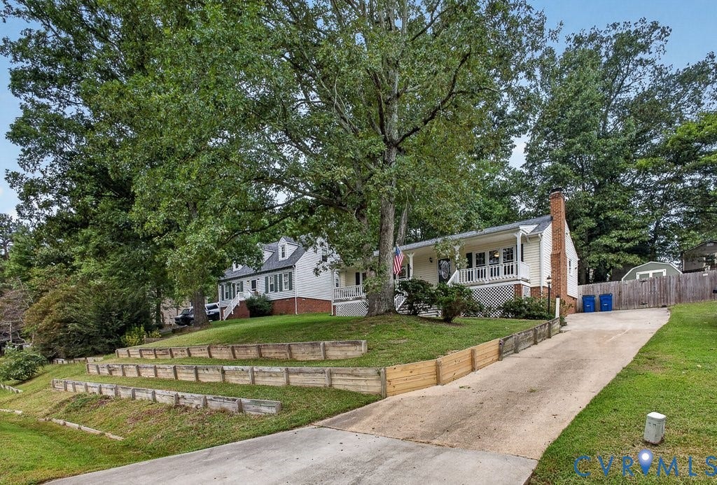 3112 Castlebury Drive, Chester, VA 23831 White siding exterior with brick foundation, front porch with white railings, mature trees, and tiered retaining walls