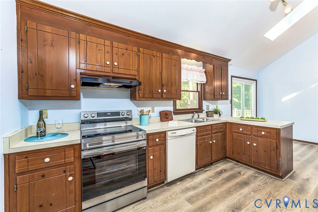 Wood-finish flooring, wood cabinetry, white countertops, stainless steel range, and a built-in dishwasher