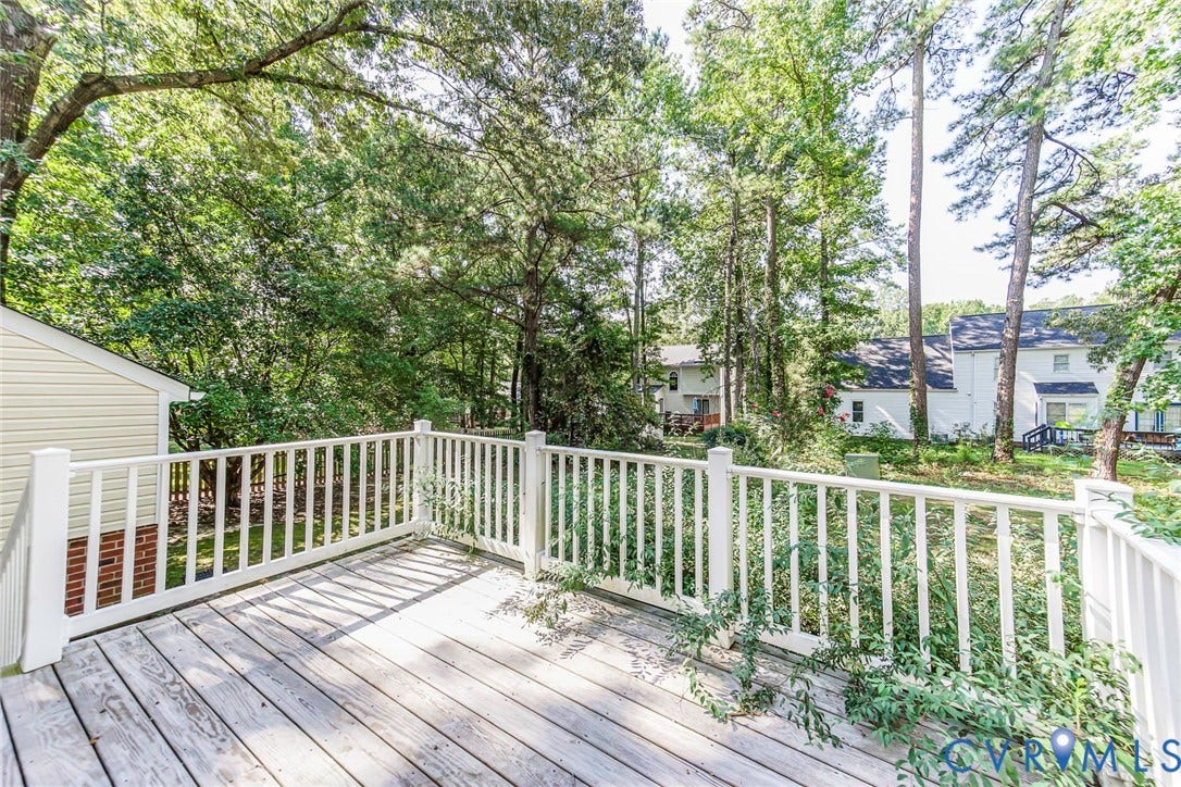 Expansive outdoor deck with white railing, wood-finish decking, and mature trees providing natural screening