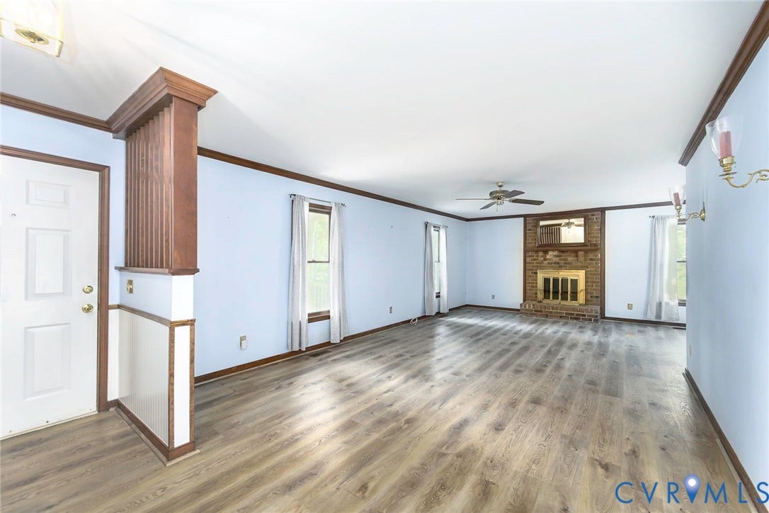 Spacious room featuring wood-finish flooring, a brick fireplace with a gold-tone screen, a ceiling fan, and multiple windows