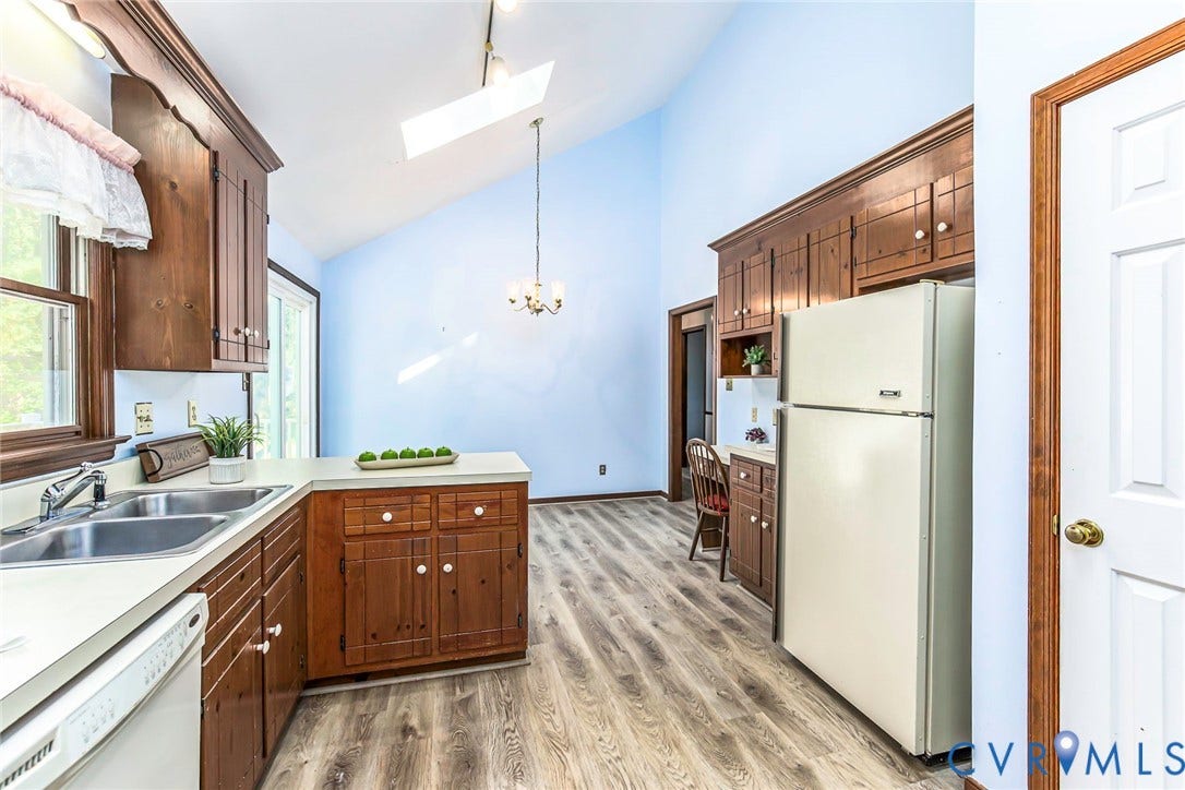Kitchen featuring wood cabinetry, light countertops, wood-finish flooring, a vaulted ceiling, and a skylight