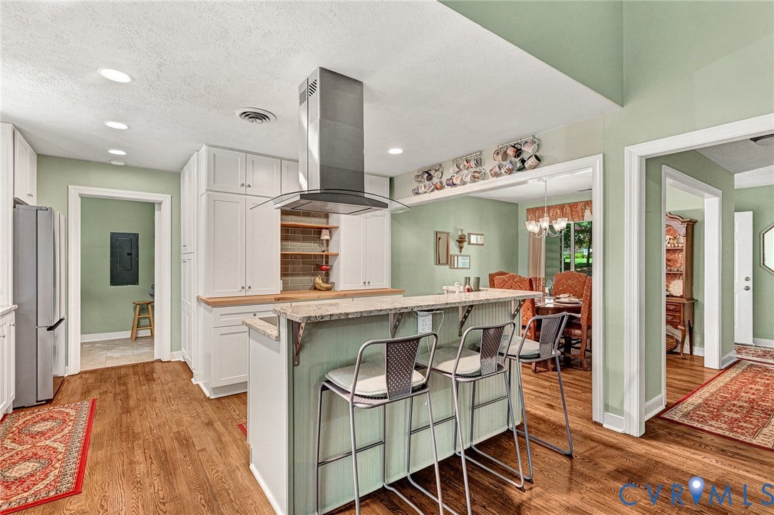 Kitchen featuring a central island with counter seating, built-in cooktop with stainless steel range hood, recessed lighting, and wood-finish flooring