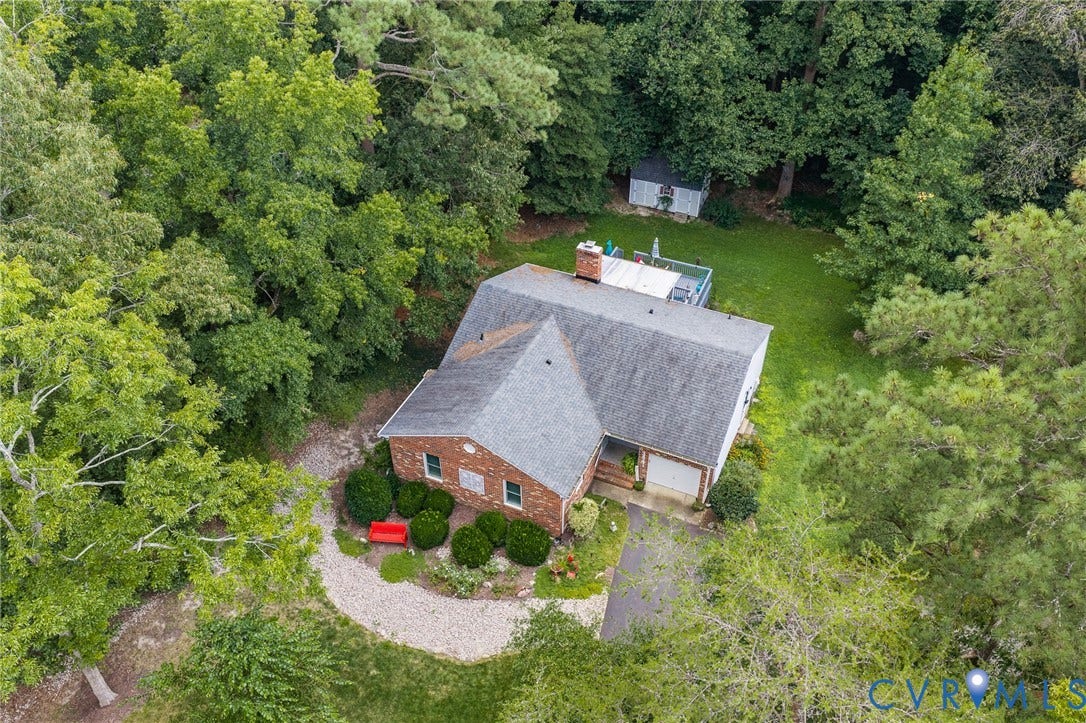 Brick exterior with an attached garage, featuring a gravel pathway, mature landscaping, and an expansive backyard with a detached shed