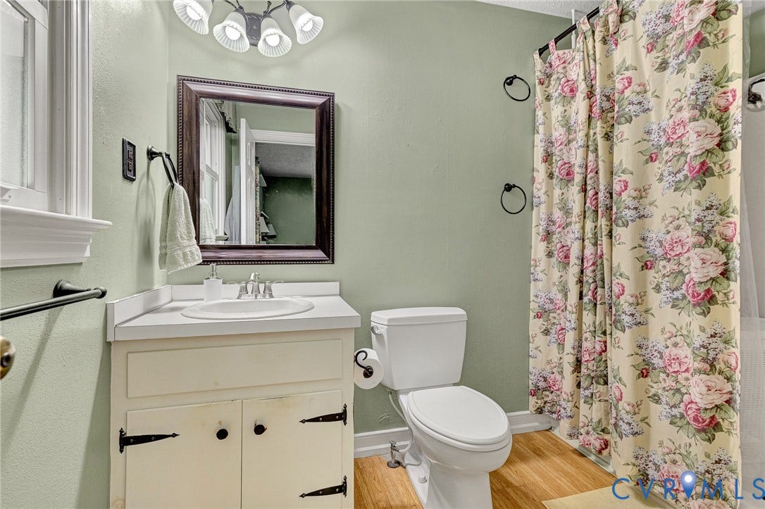 Wood-finish flooring, white vanity with integrated sink, framed mirror, and a white toilet