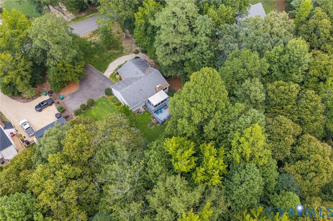 Spacious property surrounded by mature trees, featuring a private driveway, a two-story residence, and an elevated deck area