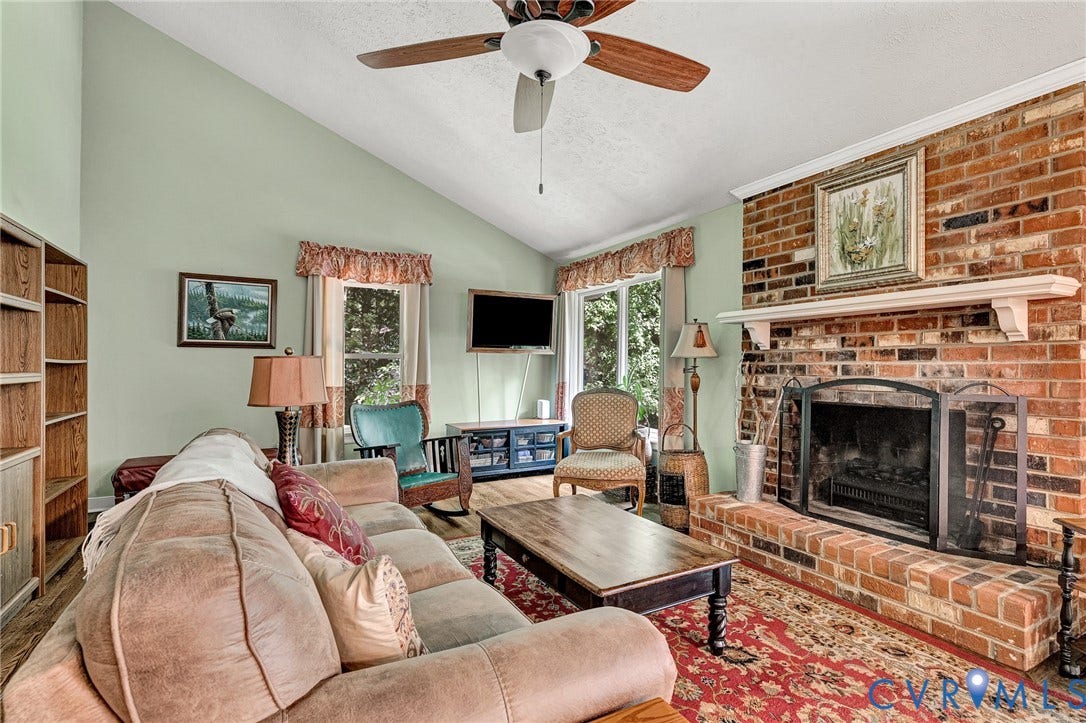 Brick-faced fireplace with a white mantle, vaulted ceiling with a ceiling fan, and built-in shelving