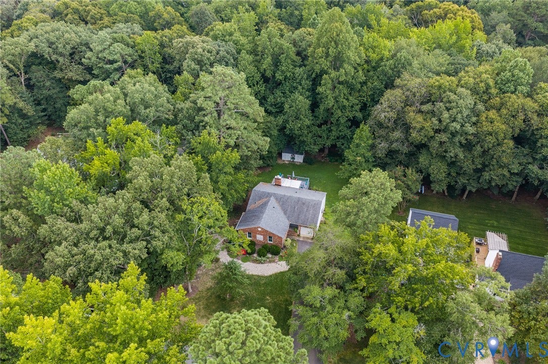 Brick exterior, gabled roof, lush mature trees, expansive green lawn, and two detached sheds