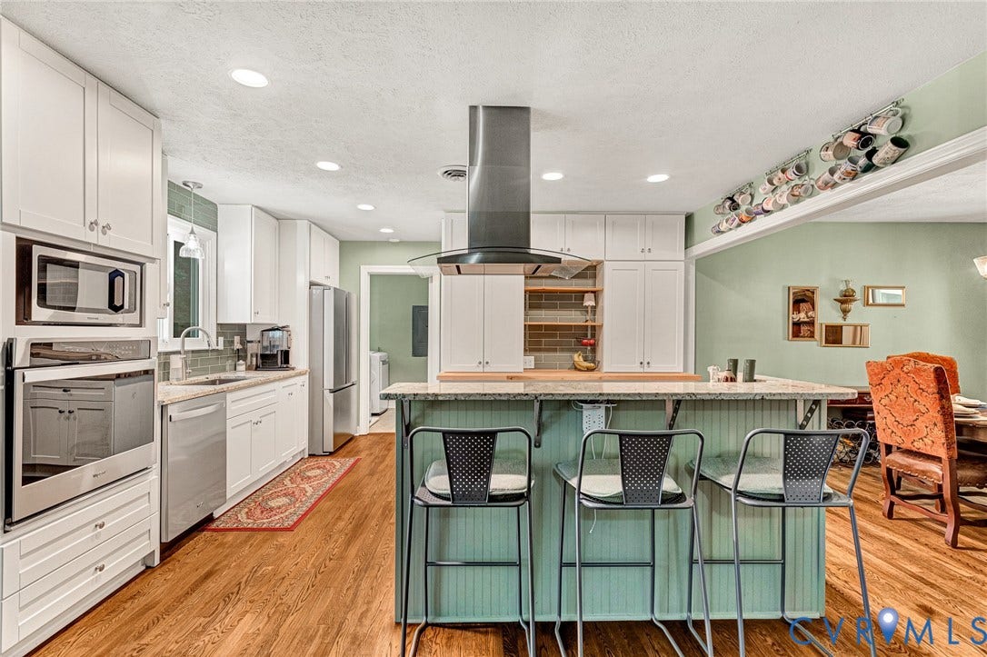 Kitchen featuring recessed lighting, wood-finish flooring, white cabinetry, integrated stainless steel appliances, and a central island with counter seating