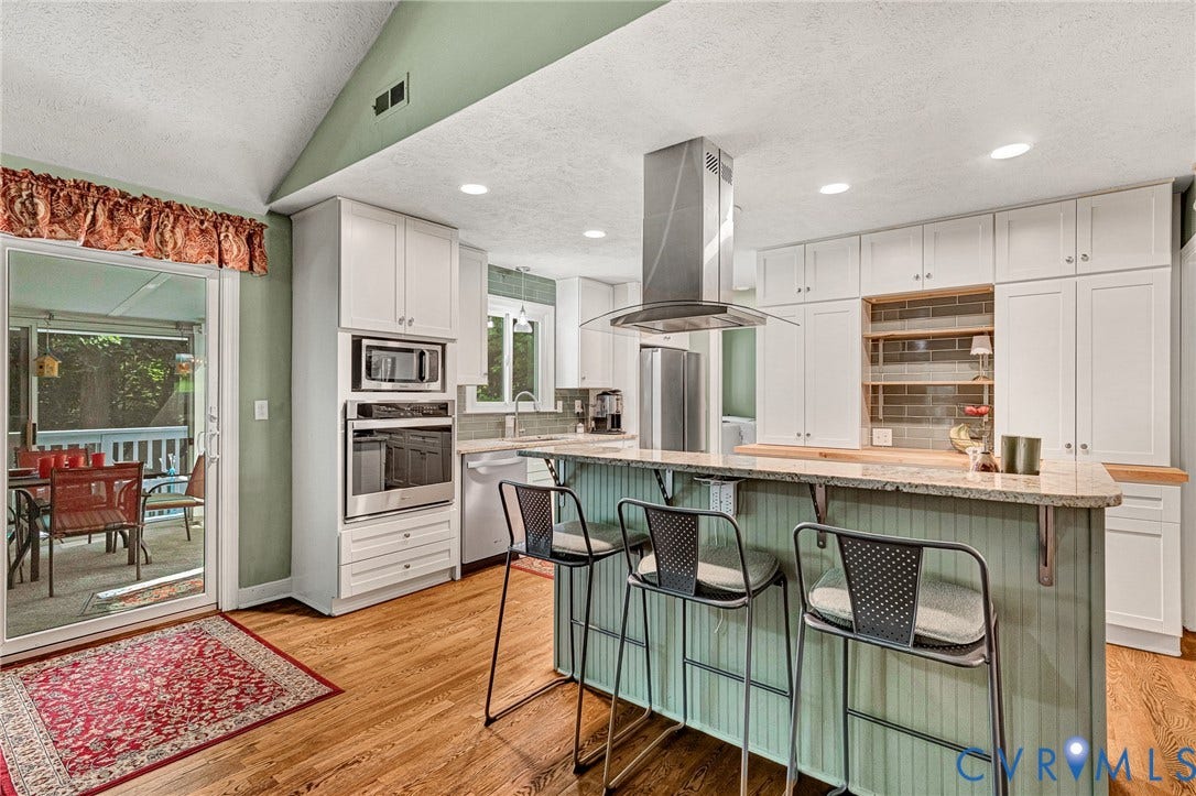 Kitchen with wood-finish flooring, white cabinetry, a built-in oven and microwave, an island with a countertop, and a sliding glass door leading to an outdoor screened porch