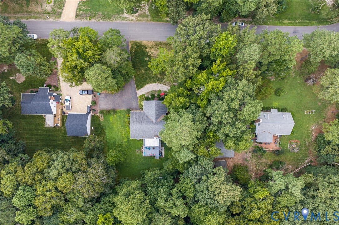 Aerial view showcasing a property surrounded by mature trees, a paved driveway, and additional outbuilding