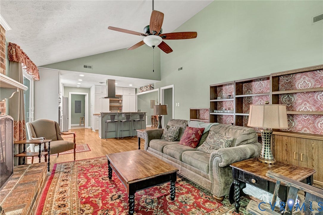 Vaulted ceilings, wood-finish flooring, built-in shelving, kitchen island with seating, and a brick-surround fireplace