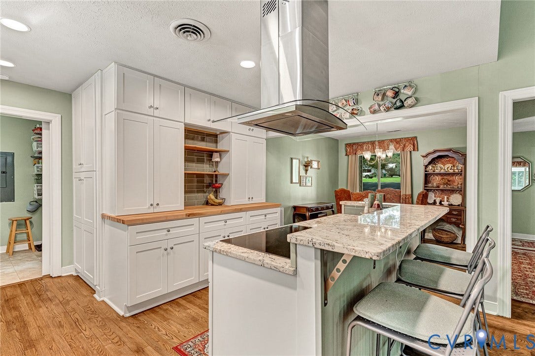 Kitchen featuring hardwood flooring, white shaker-style cabinetry, wood countertops, a stainless steel range hood, and a stone-topped island with seating