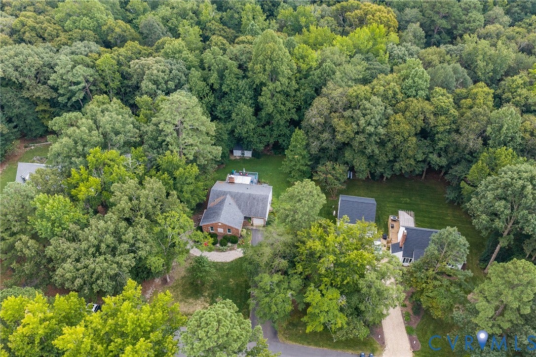 Extensive tree coverage, paved driveway, brick facade, and gabled roofline