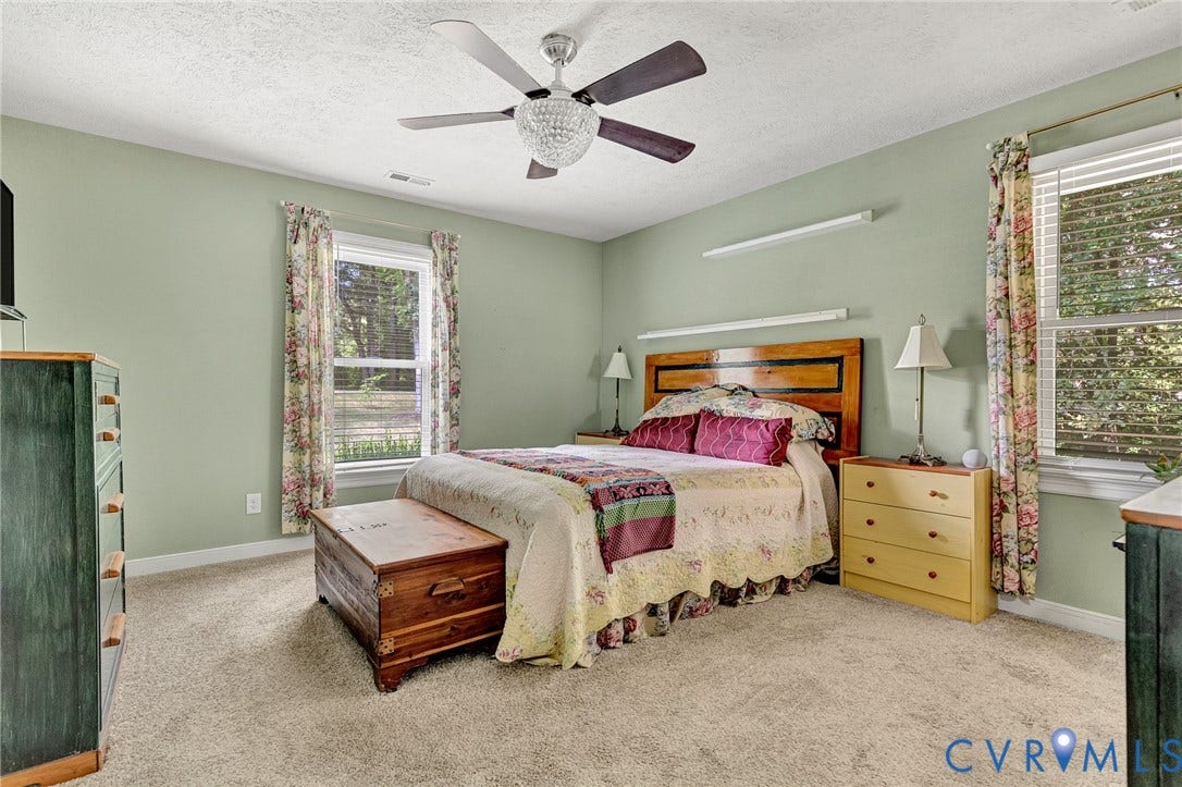 Carpeted bedroom with two windows, a wood headboard, and a ceiling fan with an integrated light fixture