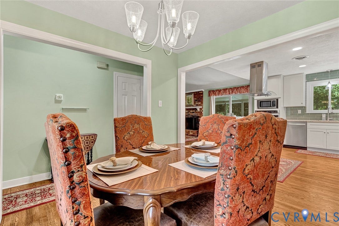 Warm wood-finish flooring throughout, a decorative chandelier, and a spacious archway to the kitchen