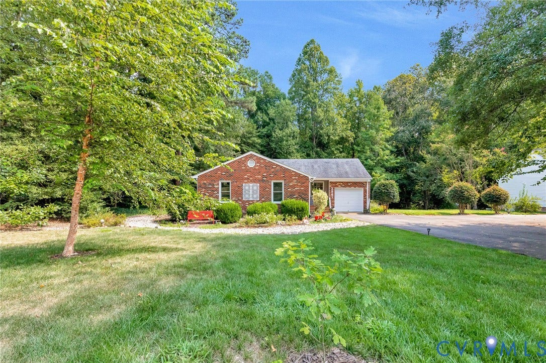 Brick exterior, attached garage, paved driveway, mature trees, landscaped shrubbery