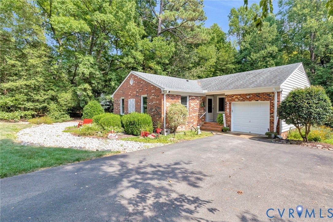Brick and siding exterior with a shingled roof, featuring an attached single-car garage, a paved driveway, and established landscaping