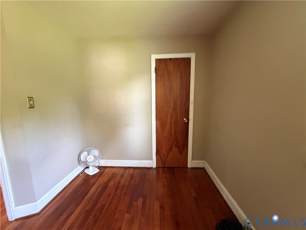 Wood-finish flooring with white trim, solid core wood door, and neutral wall tones
