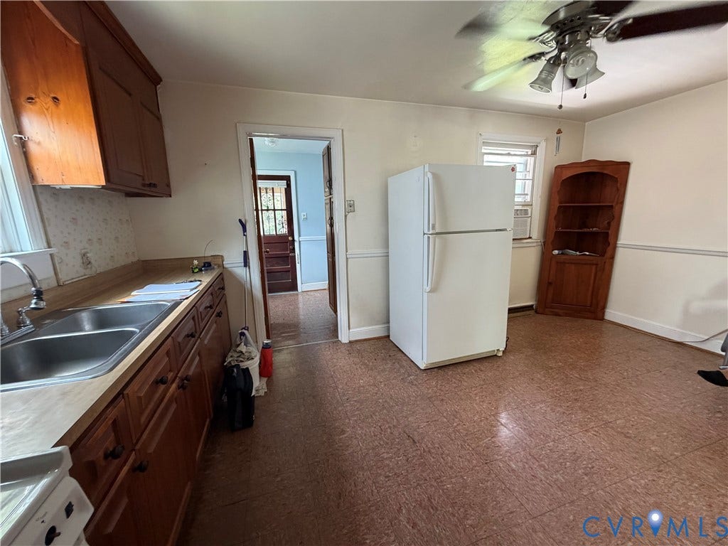 Efficient kitchen space featuring wood cabinetry, a double basin stainless steel sink, and a ceiling fan with integrated lighting