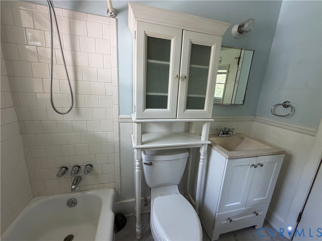 Bathtub with subway tile surround, over-toilet storage cabinet, vanity with integrated sink, and wall-mounted mirror