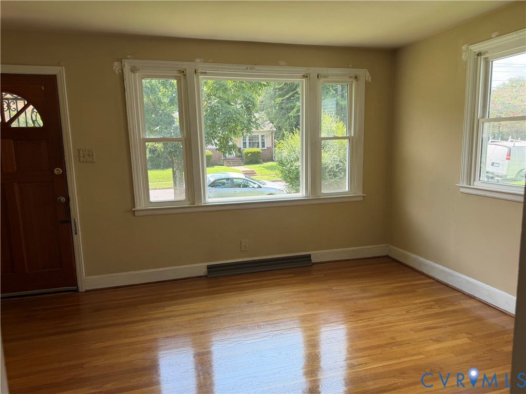Wood-finish flooring, multiple windows with white trim, and a wood-panel entry door with decorative ironwork