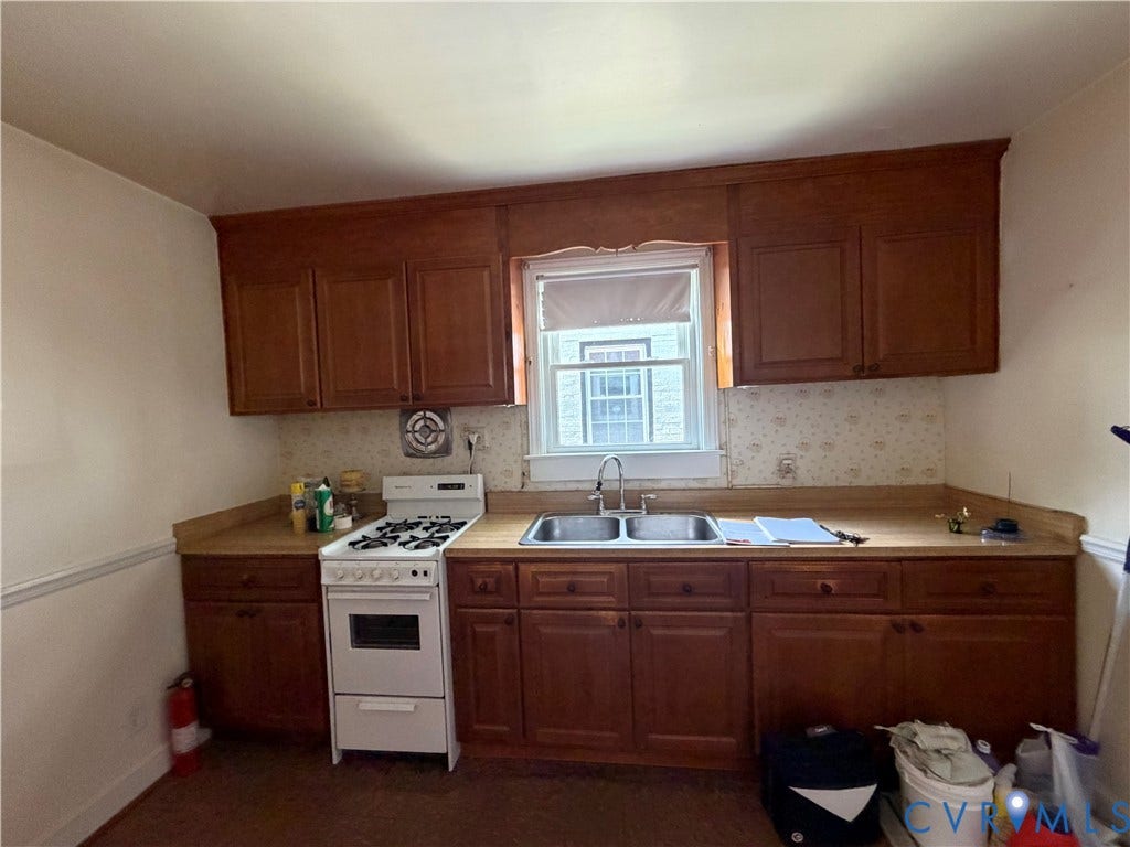 Wood-finish cabinetry, dual basin stainless steel sink, white gas range, and a window with natural light