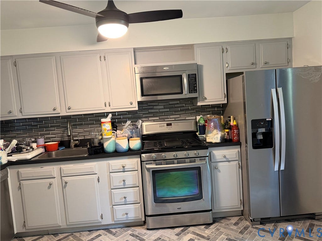 Gray cabinetry with brushed nickel hardware, stainless steel appliances, dark countertop, subway tile backsplash, and herringbone-patterned flooring
