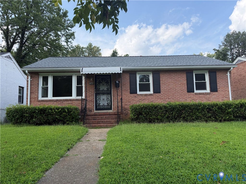 Brick exterior with dark shutters, a covered entry, and a manicured front lawn