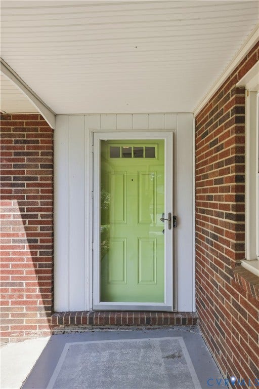 Brick exterior with a covered entryway, showcasing a bright green front door with an overhead transom window, and a full-light storm door