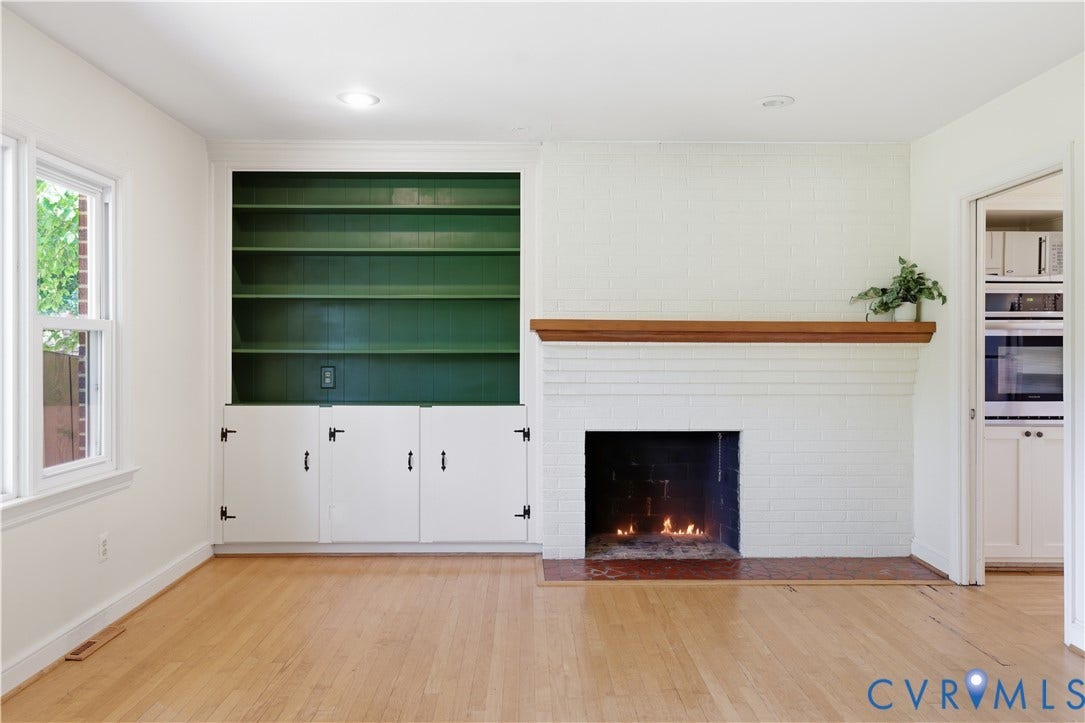 Wood-finish flooring, white brick wood burning fireplace with wood mantel, built-in shelving with lower cabinetry