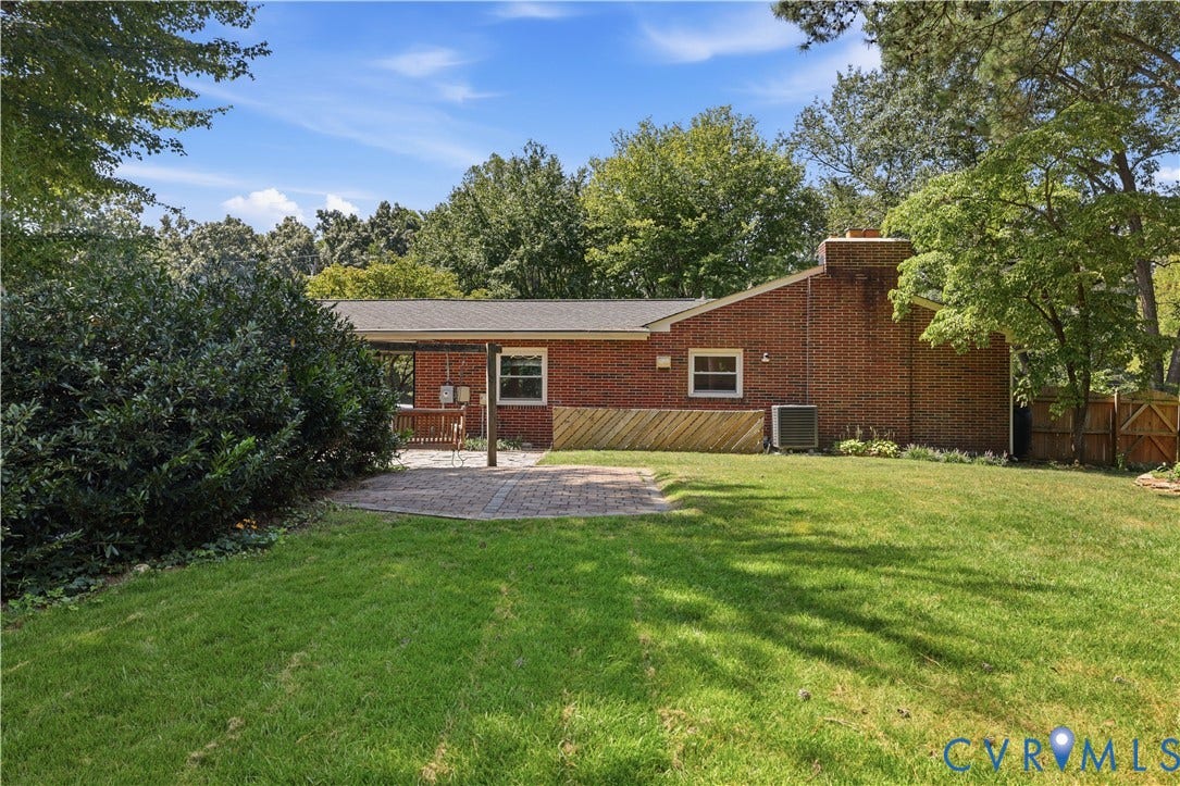 Brick exterior with a covered patio, paved patio area, and a lush lawn